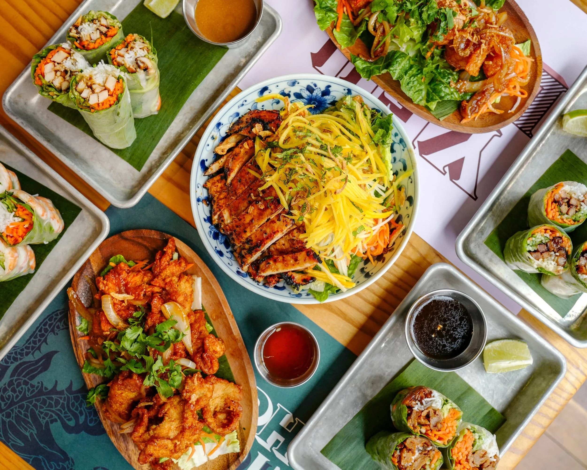 Overhead spread of grilled chicken rice bowl, spring rolls, and drinks